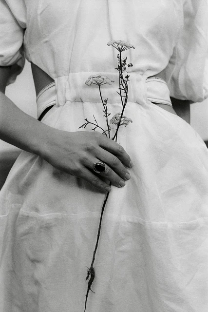 Monochrome image: A woman in a white dress holds white Queen Anne's lace flowers in her hand with a ring, soft lighting.