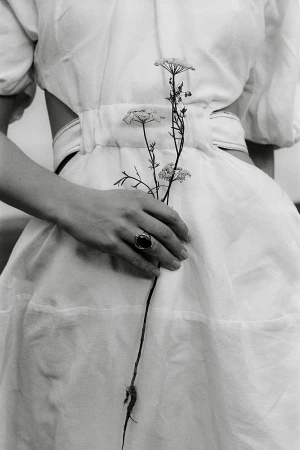 Monochrome image: A woman in a white dress holds white Queen Anne's lace flowers in her hand with a ring, soft lighting.