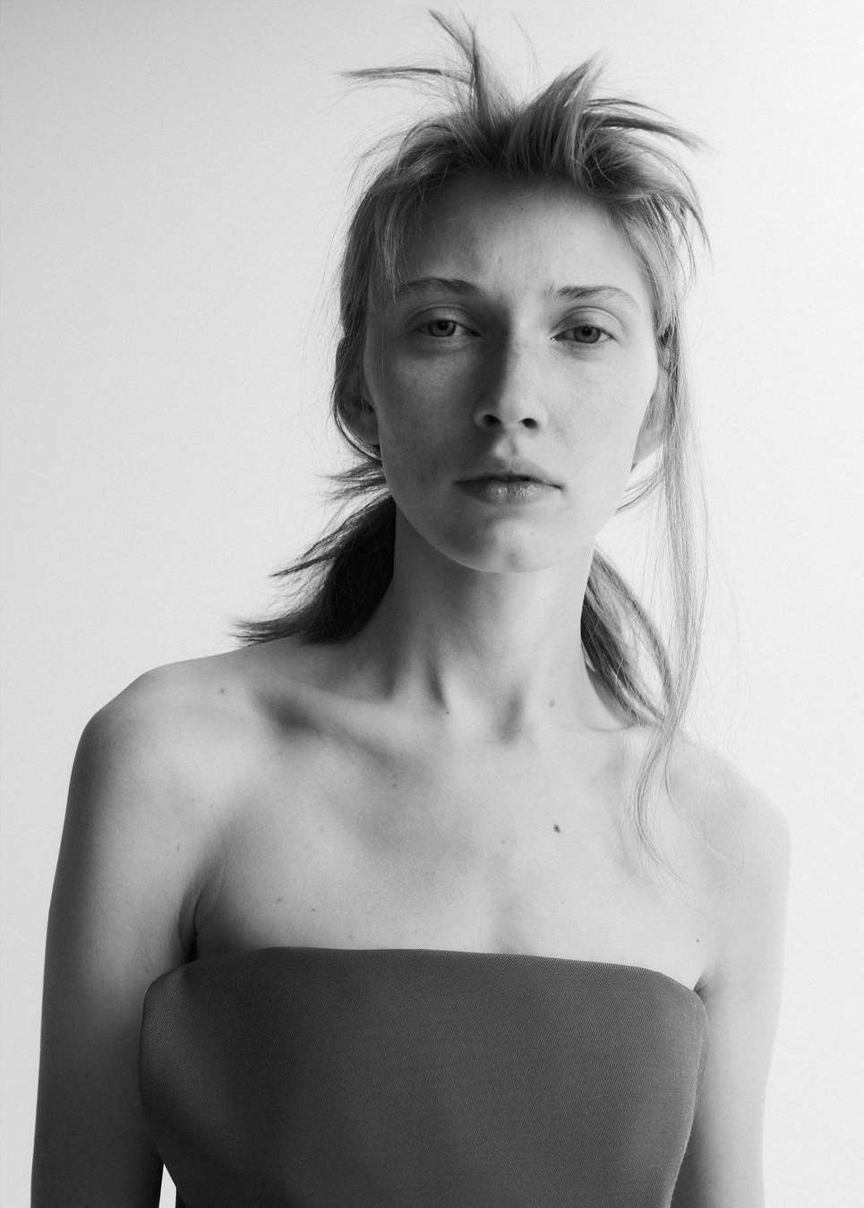 Monochrome portrait of a woman with tousled hair wearing a strapless top against a seamless white background.