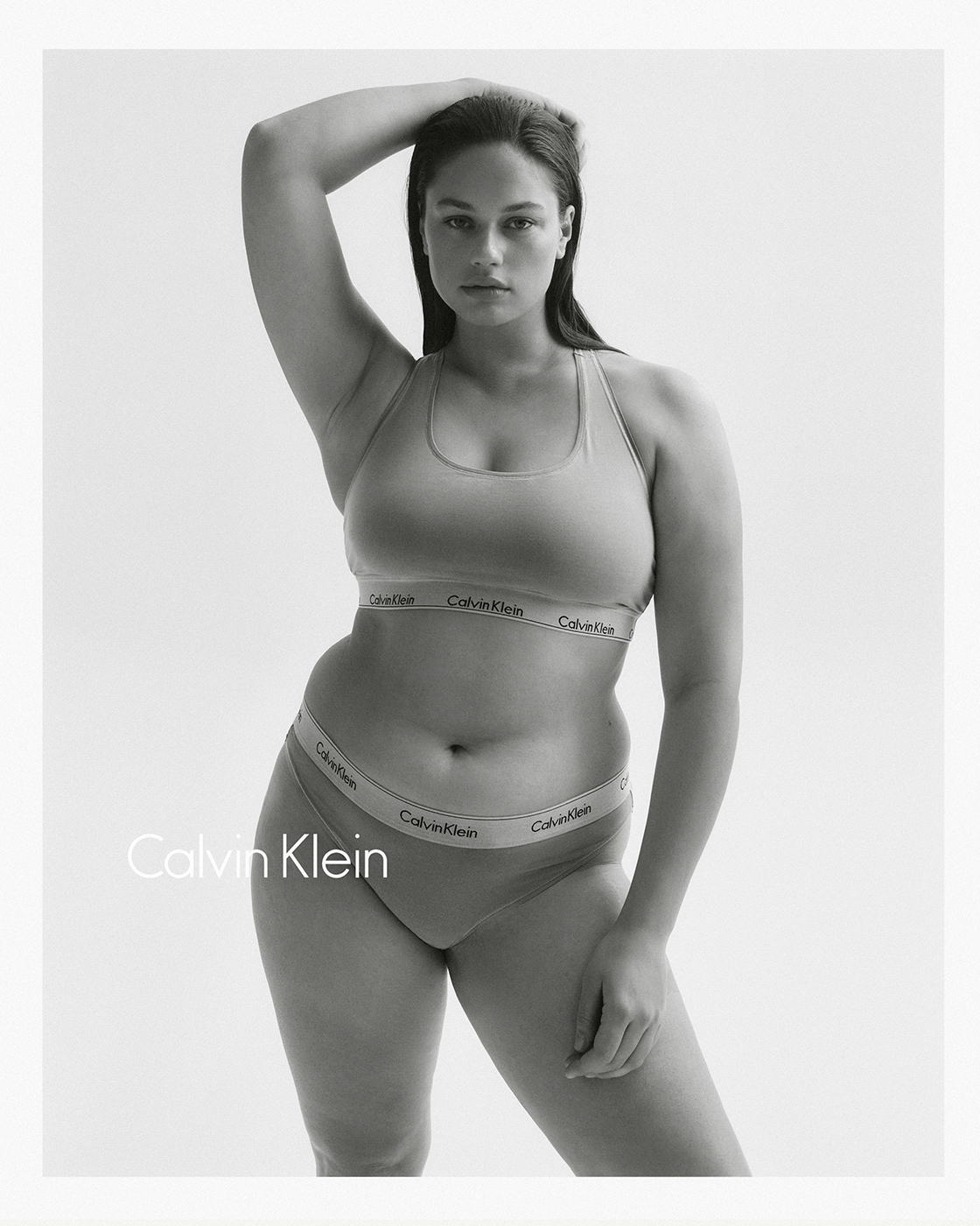 Black-and-white portrait of a curvy woman in underwear posing against a white background with the Calvin Klein logo visible.