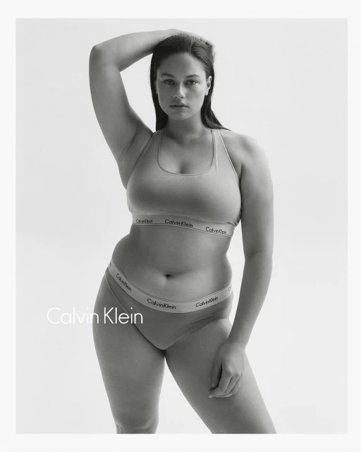 Black-and-white portrait of a curvy woman in underwear posing against a white background with the Calvin Klein logo visible.