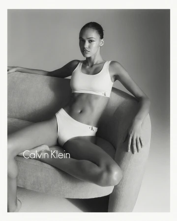 Monochrome portrait of a female model seated on a curved sofa wearing white underwear by Calvin Klein.