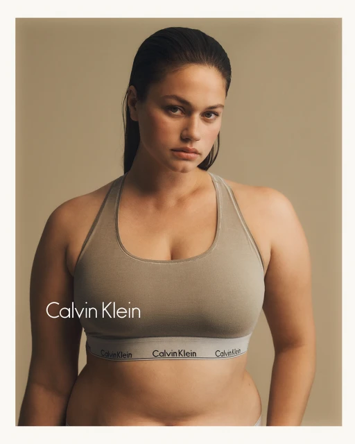 A portrait of a plus-size woman wearing a Calvin Klein sports bra with a serious expression. The image is a close-up shot with a neutral background.