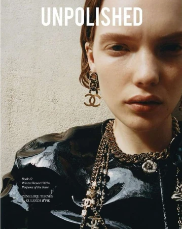 Close-up portrait of a young woman in a glossy black jacket adorned with gold Chanel jewelry, as featured on the cover of Unpolished.