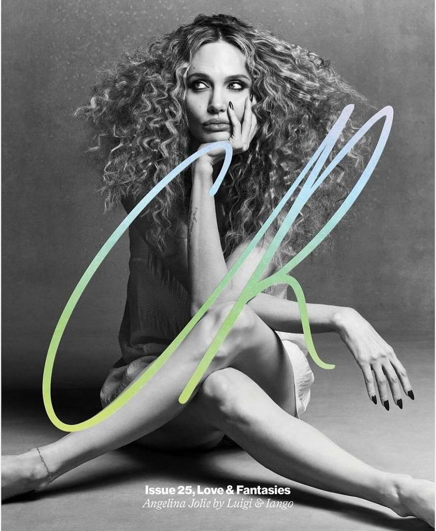 Monochrome magazine cover shot of Angelina Jolie with curly hair, sitting cross-legged, leaning on her hand, with large stylized text.