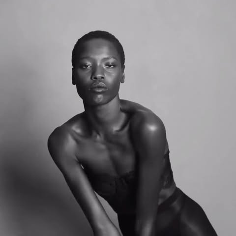 Portrait of a black woman with short hair in dark clothing, against a light grey background, demonstrating a sensual, confident pose.