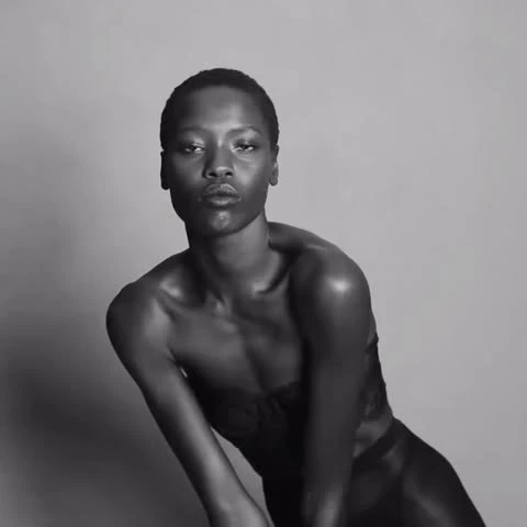 Portrait of a black woman with short hair in dark clothing, against a light grey background, demonstrating a sensual, confident pose.