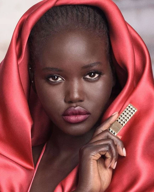 A dark-skinned female model presents beauty product, featuring deep skin tone, soft lighting, and focus on lipstick and makeup.