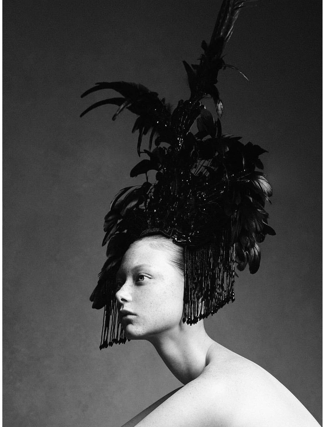 Monochrome portrait of a woman wearing an elaborate feathered headpiece. The image showcases beauty and high-fashion editorial style.