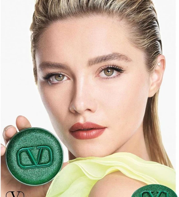 Close-up beauty shot of a blonde woman holding a green Valentino makeup compact, showcasing elegant makeup and stylishly slicked-back hair.