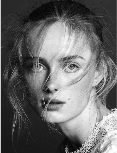 Monochrome portrait of a fair-skinned woman with freckles and light hair, close-up with a shallow depth of field, set against a dark background.