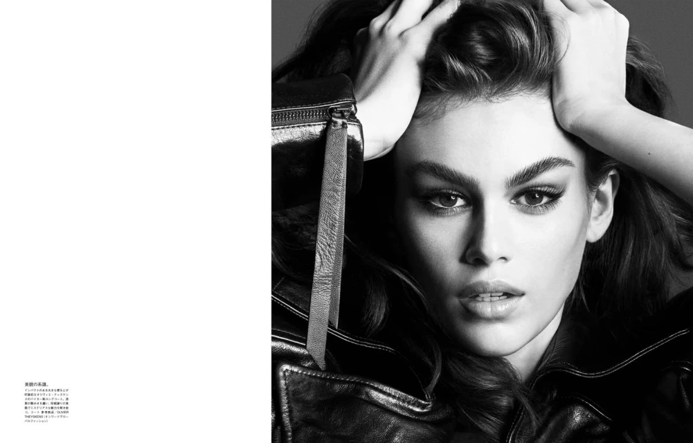 Black and white portrait of a woman with her hands in her hair, wearing a leather jacket with a zipper pull.