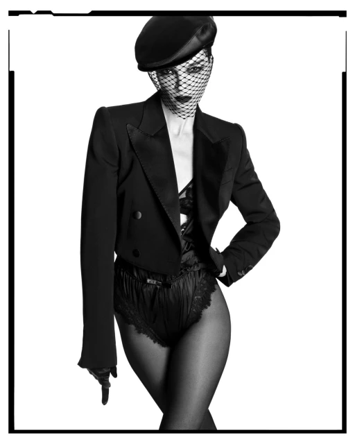 Monochrome studio portrait of a stylish woman wearing a black beret with net veil, cropped jacket, and lace-trimmed bottoms against white.