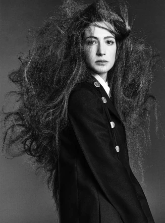 Monochrome portrait of a woman with voluminous textured hair wearing a dark buttoned coat.