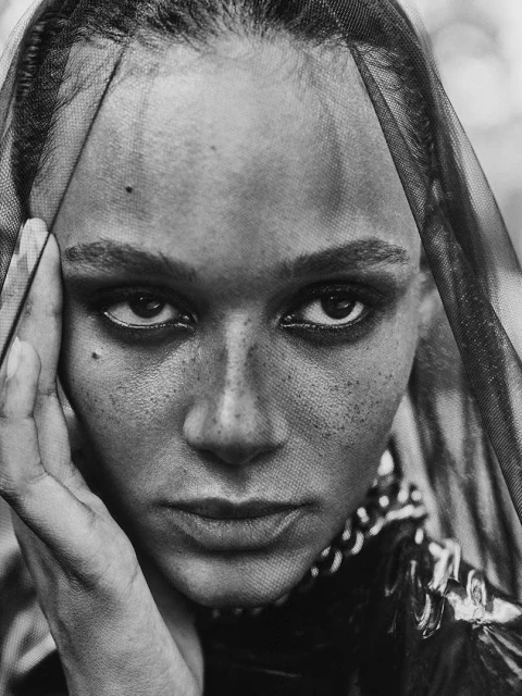 Close-up portrait of an African American adult female with freckles and a veil, creating a dramatic fashion editorial image.
