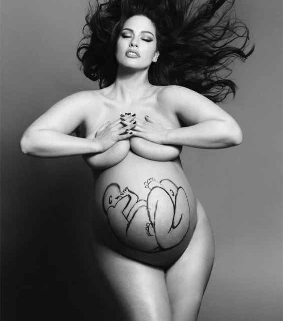 Monochrome portrait of a pregnant model, Ashley Graham, standing in a photo studio with hands on her chest and illustration on her belly.