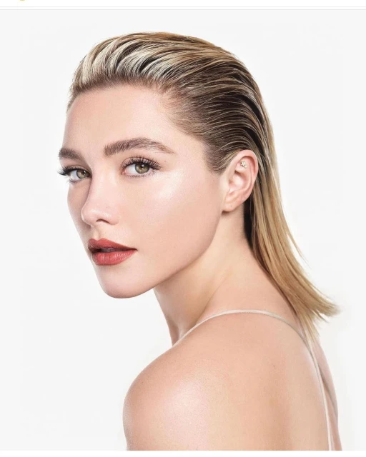 Close-up portrait of a fair-skinned adult female with blonde slicked-back hair, red lipstick, against a clean, bright white background.