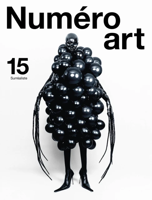 Fashion editorial shot of a model wearing a black balloon dress and black heels for Numero art magazine against a white background.