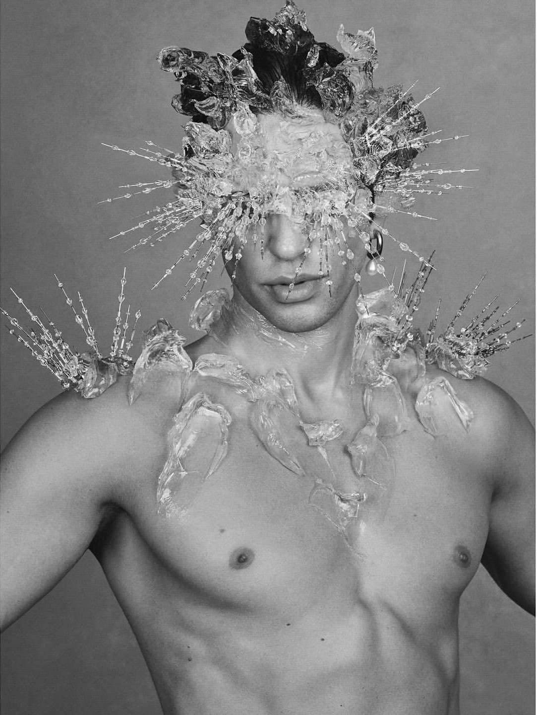 Striking black and white portrait of a shirtless adult male model adorned with ice-like sculptural elements around his head and shoulders.