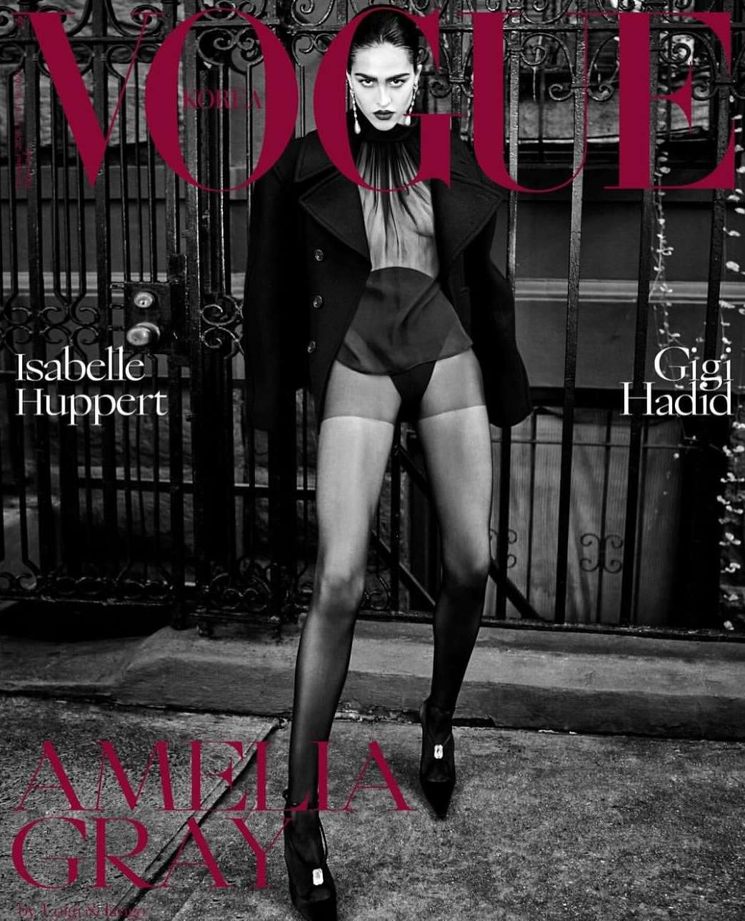 Fashion magazine cover featuring a model in a black coat and sheer lingerie, set against a wrought iron fence and city street backdrop.