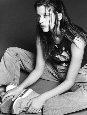 Monochrome portrait of a young woman with wet-look hair sitting on the floor wearing graphic t-shirt and loose denim jeans.