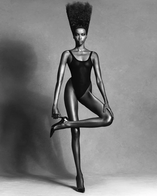 Elegant black and white portrait of a fashion model in a bodysuit, balancing on one leg while holding a high-heeled shoe.