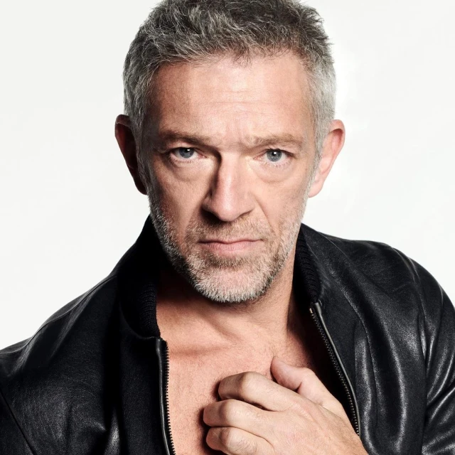 Close-up portrait of a mature adult male with salt and pepper hair, wearing a black leather jacket and posing in a photo studio.