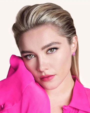 Close-up portrait of actress Florence Pugh with slicked-back blonde hair wearing a bright pink buttoned shirt.