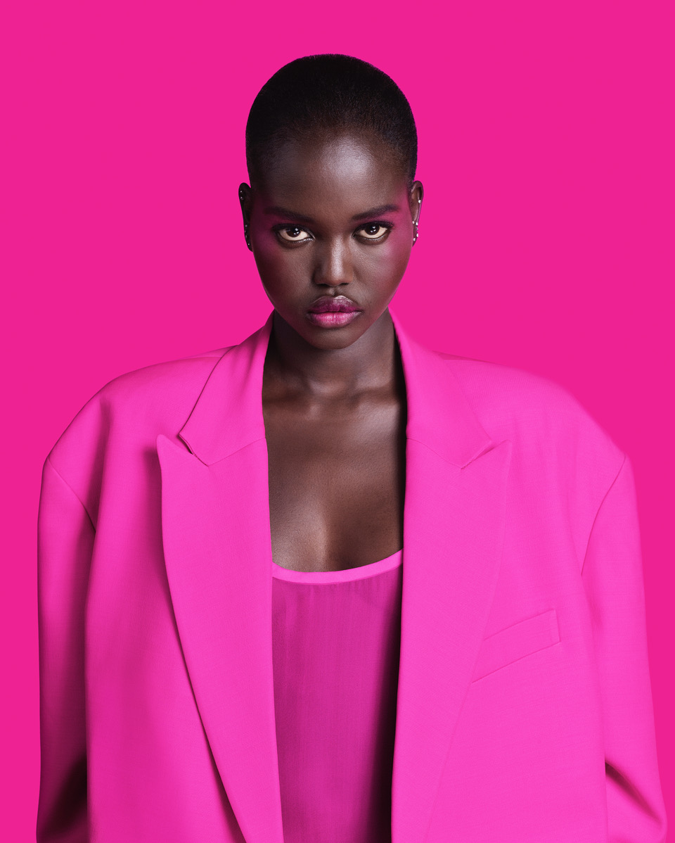 Close-up portrait of a Black woman with short hair wearing a pink blazer against a bright pink backdrop, fashion-forward and striking.