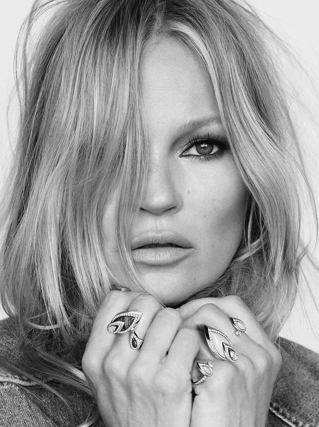 Close-up black and white portrait of Kate Moss wearing statement rings with her hands held near her chin.