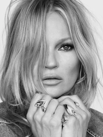Close-up black and white portrait of Kate Moss wearing statement rings with her hands held near her chin.