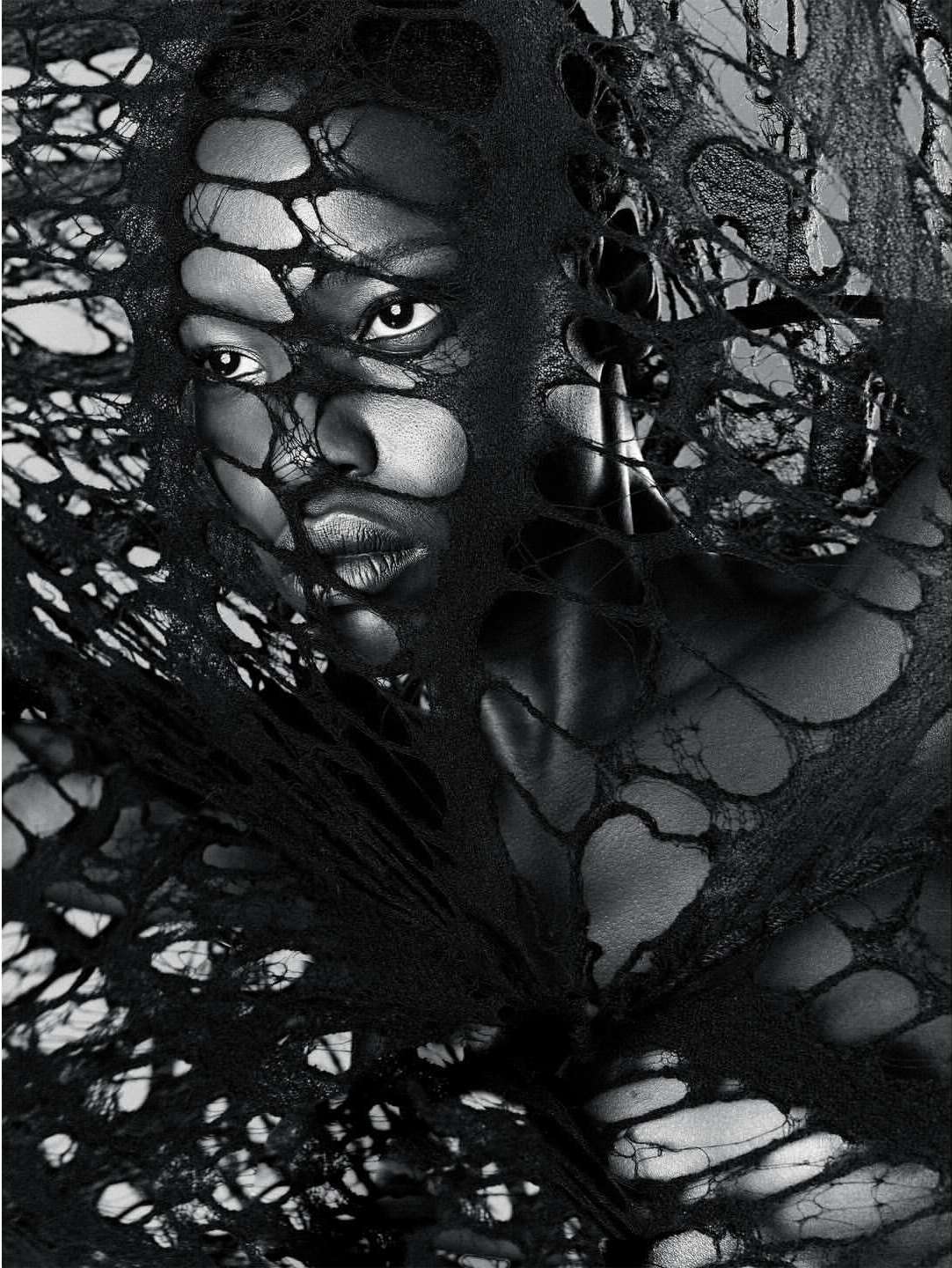 Monochrome portrait of an adult woman with short hair, wearing a dark garment with holes, against a light background in a studio.