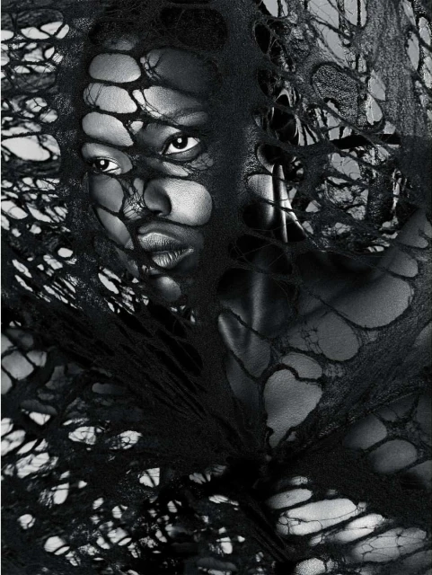 Monochrome portrait of an adult woman with short hair, wearing a dark garment with holes, against a light background in a studio.