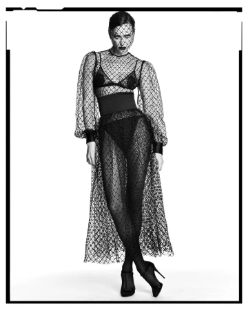 Model in black mesh netted dress and veil standing against white background by Luigi and Iango