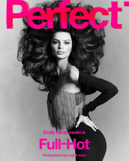 Emily Ratajkowski on a magazine cover with large voluminous dark hair, black dress and silver fringe on light gray background.