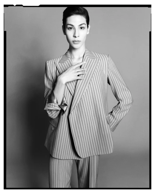 Monochrome portrait of a woman in a striped suit, posed against a gray backdrop, featuring classic tailoring and a contemporary style.