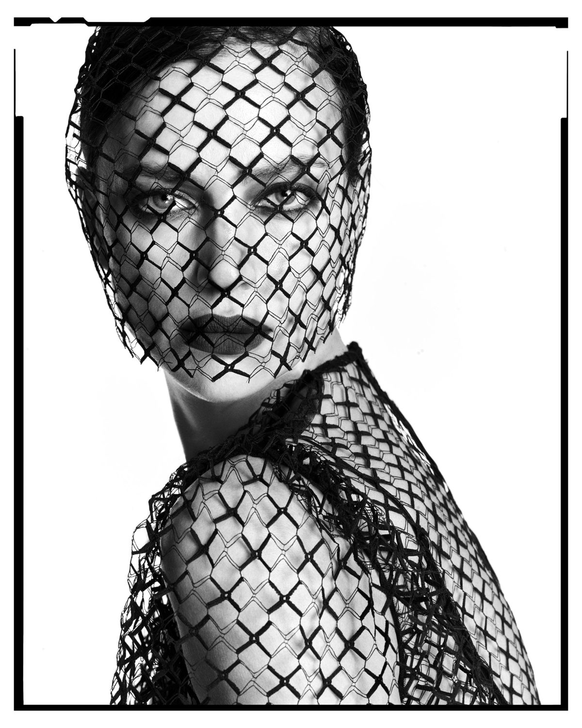 Monochrome portrait of a woman wearing a black lace veil; she is gazing directly at the camera, with a light skin tone.