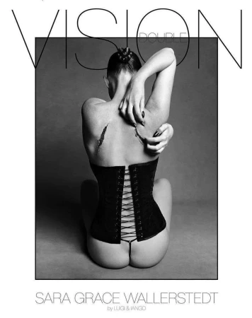 Monochrome studio shot of a woman with a styled updo, wearing a corset, and posed with her back to the camera against a grey background.
