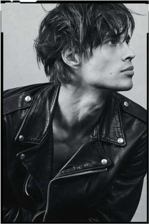 Monochrome portrait of a fair-skinned adult male fashion model wearing a black leather jacket, looking off-camera in a studio setting.