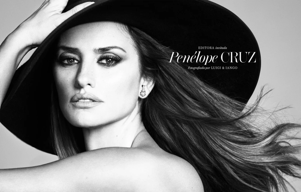 Close-up black-and-white portrait of Penélope Cruz wearing a wide-brimmed hat, gazing at the camera with long hair and heavy eye makeup.