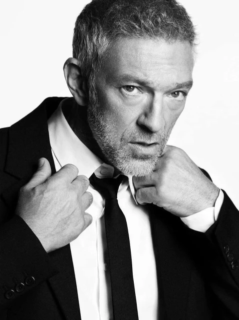 Portrait of adult male with gray hair, wearing a dark suit and tie against a white backdrop. Focus on face and upper torso.