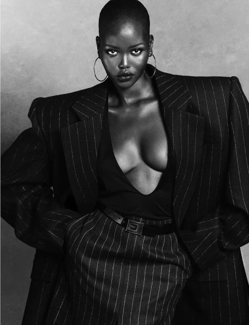 Black and white portrait of an African American female model wearing a pinstripe suit and hoop earrings looking at the camera.