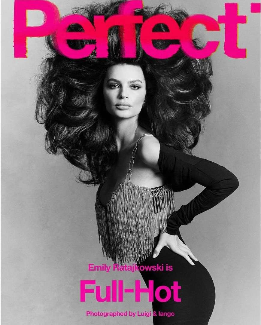 Emily Ratajkowski poses on a magazine cover with large, dark curly hair, wearing a black dress and a silver, fringed top.
