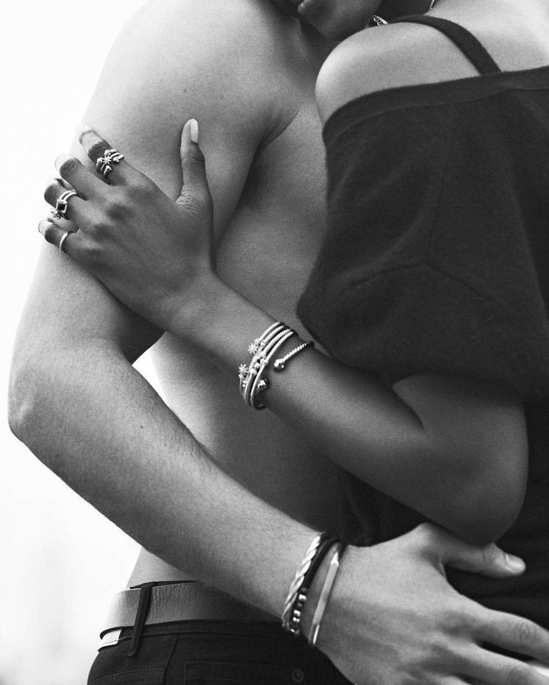 Close-up monochrome portrait of two people embracing, wearing multiple silver rings and bracelets by Matthew Brookes.