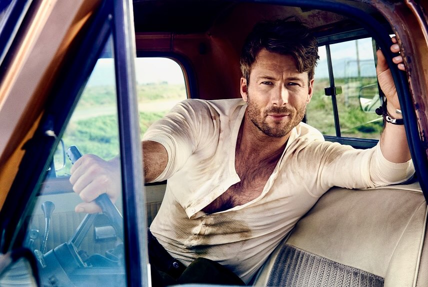Portrait of a handsome adult male inside a vintage truck, wearing a white shirt, with a green rural landscape in the background.