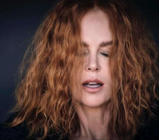 Close-up portrait of Nicole Kidman with wavy red hair and parted lips against a dark background