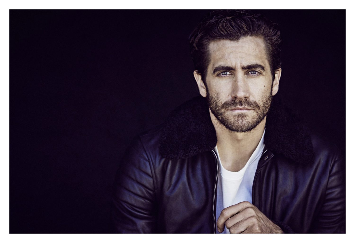 Portrait of actor Jake Gyllenhaal wearing a black leather jacket with a dark shearling collar over a white t shirt.