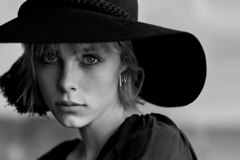 Black-and-white portrait of a young woman with short blonde hair and a wide-brimmed hat looking directly at the camera with a neutral expression.