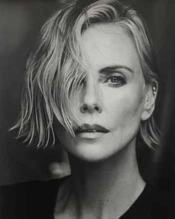 Monochrome portrait of adult woman with short, layered blonde hair, fair skin, and dark eyes, in a close-up headshot against a dark backdrop.