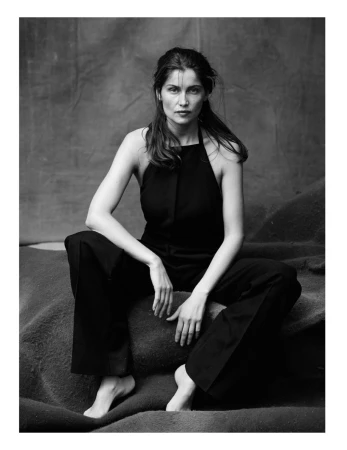 Black and white portrait of a woman in a dark halter top and trousers seated on a draped textured studio backdrop.